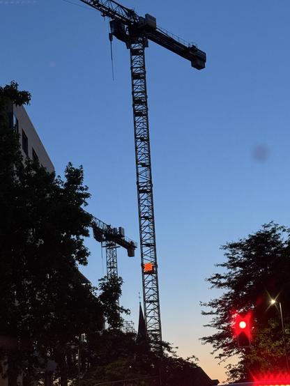 Zwei Baukräne vor Abendhimmel. Rechts im Vordergrund eine rote Ampel