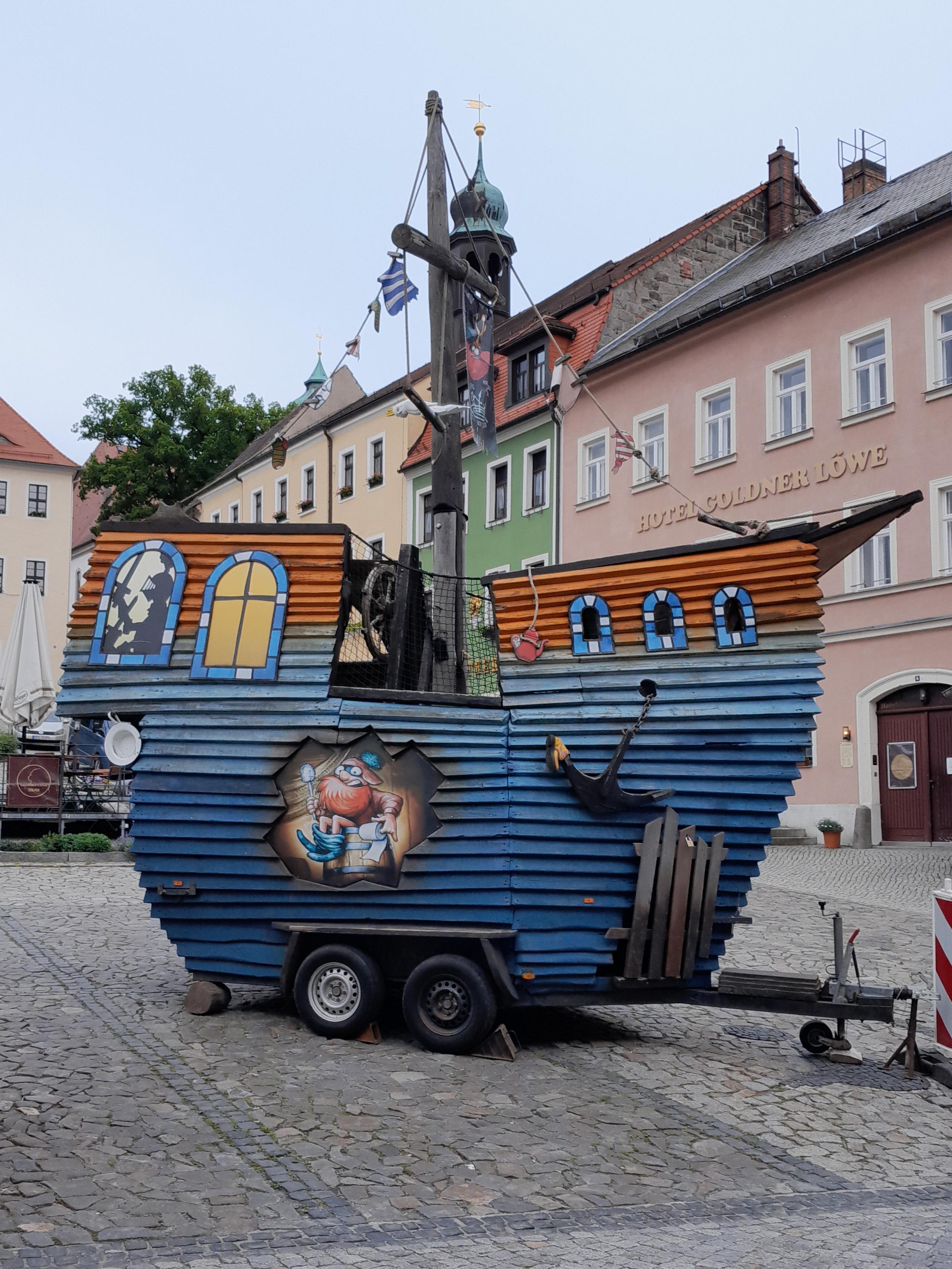 Ein großes Schiff aus Holz, bunt angemalt, zum Transport hat es Räder und Deichsel. Es steht auf einem gepflasterten Platz, im Hintergrund sieht man Häuser. Es dient als Spielschiff für Kinder und stand bei uns zum Stadtfest. Ein großes Schiff aus Holz, bunt angemalt, zum Transport hat es Räder und Deichsel. Es steht auf einem gepflasterten Platz, im Hintergrund sieht man Häuser. Es dient als Spielschiff für Kinder und stand bei uns zum Stadtfest.